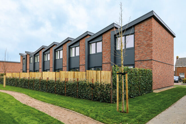 Nieuwbouw Heerewaarden met opvallende zaagtanddaken, antraciete UniKern® geveldetails en rode gevelstenen.